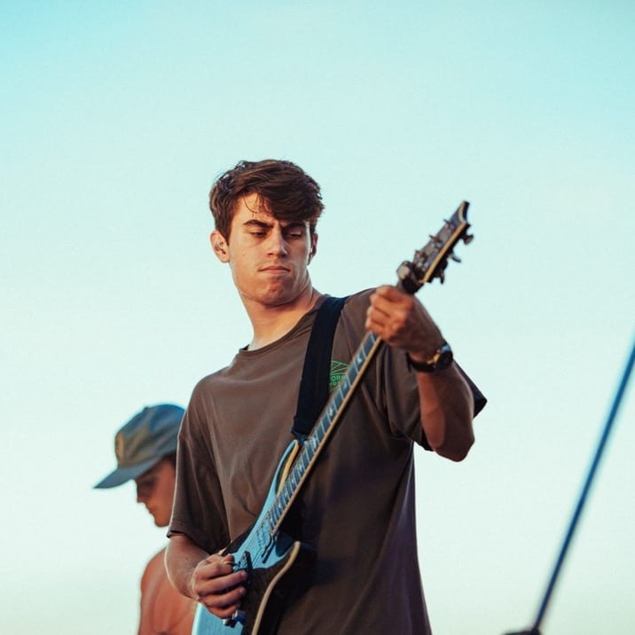 Nick Troiano, Founder & Lead Engineer, playing guitar on an outdoor stage at sunset